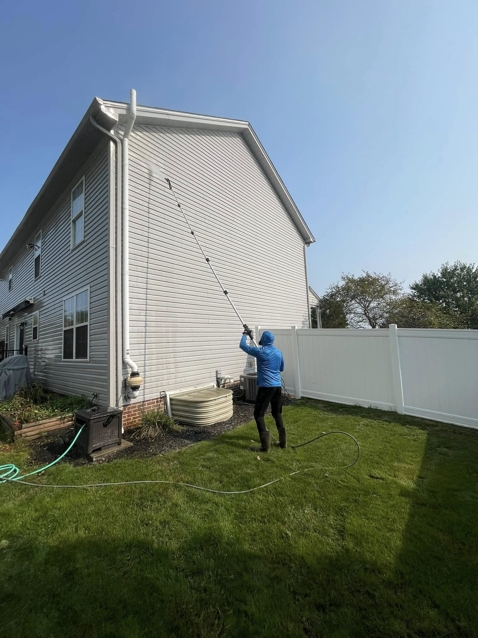 Worker pressure washing light gray vinyl siding with an extension wand