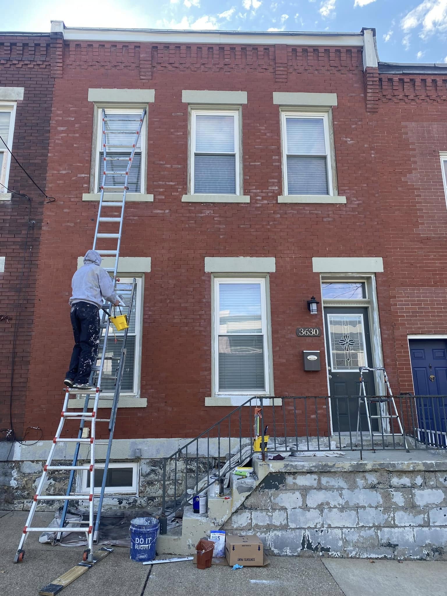 Painter working on exterior brick house trim from a ladder