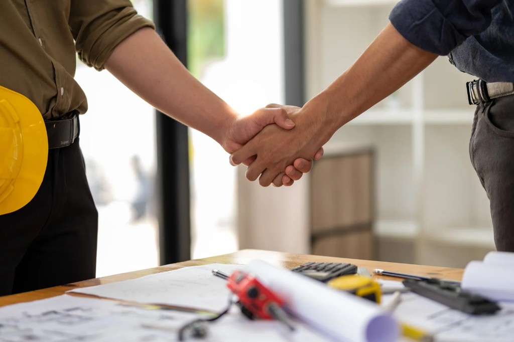 Business handshake over construction plans on a desk